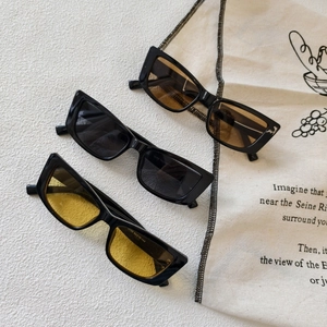 Three retro square sunglasses in brown, grey, and yellow lenses on a beige fabric bag