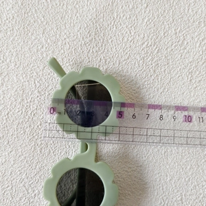 Dettaglio occhiali da sole a fiore verde chiaro per bambini con righello di misura