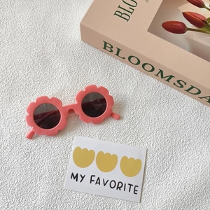 Dettaglio degli occhiali da sole a forma di fiore rosa per bambini su sfondo crema
