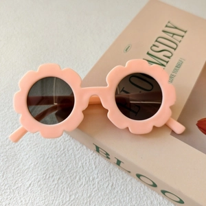 Occhiali da sole per bambini a forma di fiore rosa opaco su sfondo di un libro