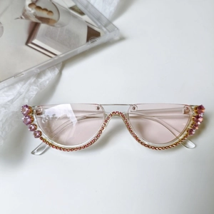 Détail de lunettes de soleil œil-de-chat roses avec strass et décorations en pierres violettes