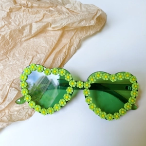 Detail shot of heart-shaped green sunglasses featuring decorative 3D daisy flower frames