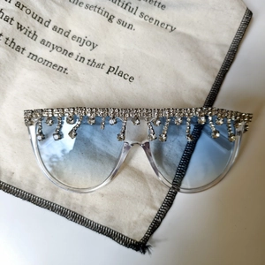 Dettaglio di occhiali da sole oversize con lenti sfumate blu e nappe di strass argento