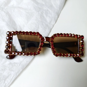 Detailed close-up of rectangular bridal sunglasses with red rhinestones and gold metal trim
