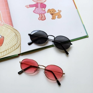 Flat lay of retro oval metal frame sunglasses in black and gold with gradient pink lenses