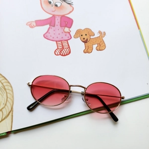 Detailed close-up of retro oval sunglasses with pink lenses and gold metal frames on artbook