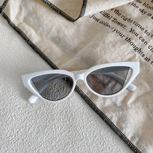 Detail of white cat eye sunglasses with grey lenses on a minimalist linen background
