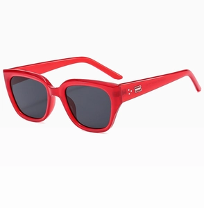 Close-up of red translucent frame sunglasses with silver metal logo and three-dot rivets