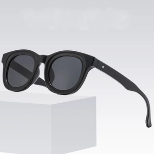 Modern black thick frame sunglasses with dark lenses on a minimalist white platform