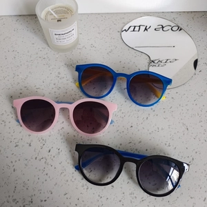 Trois paires de lunettes de soleil rondes pour enfants en bleu rose et noir sur pierre