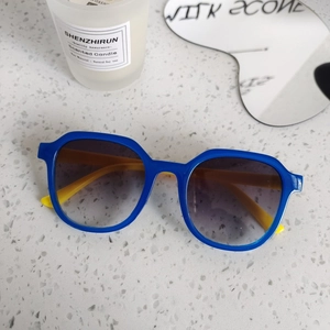 Detail of blue and yellow square sunglasses on a white terrazzo surface with a candle