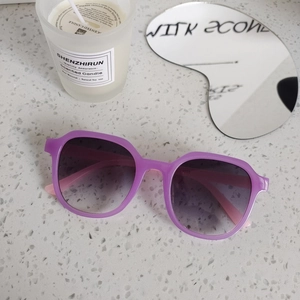 Detailed view of purple irregular frame sunglasses with grey gradient lenses on stone surface