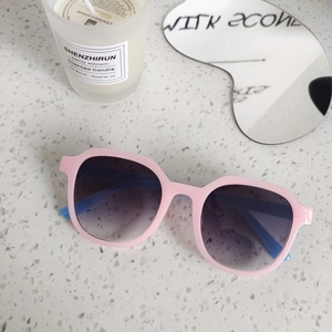 Close-up of pink matte frame sunglasses with blue arms on textured stone surface