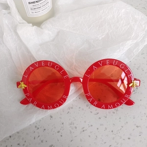 Detail of red round frame sunglasses with white lettering and gold bee accents