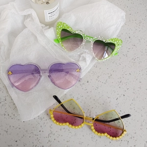 Three creative heart-shaped and wavy kids sunglasses with gradient lenses on a desk