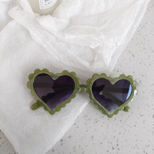 Close-up of heart-shaped sunglasses with scalloped green glitter frame and tinted lenses