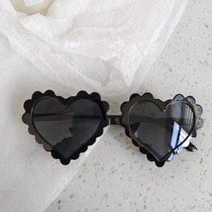 Close-up of heart-shaped sunglasses with wavy edges and black glossy frames on marble