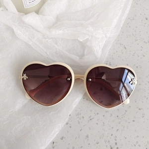 Close-up of heart-shaped sunglasses with cream frame and gold bee detail on gradient lens