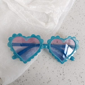 Detail of heart-shaped sunglasses with wavy blue glitter frame and gradient lenses