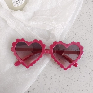 Close-up of heart-shaped sunglasses in sparkly pink with wavy scalloped frame edges