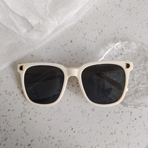 Détail de lunettes de soleil rondes blanc crème avec décoration métallique dorée en D