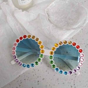 Détail de lunettes de soleil rondes blanches avec strass arc-en-ciel et verres bleus