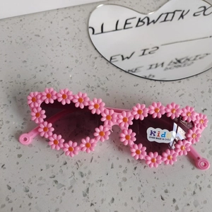 Dettaglio macro di occhiali da sole bimbi con lenti UV400 e montatura a fiori rosa
