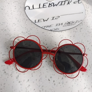 Dettaglio di occhiali da sole per bambini a forma di fiore rosso con lenti tonde scure
