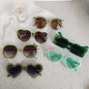 Collection of retro green kids cat-eye and heart-shaped sunglasses on white stone
