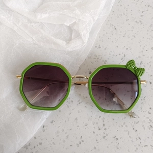 Detail view of green octagonal kids sunglasses with bow accent and gradient lenses