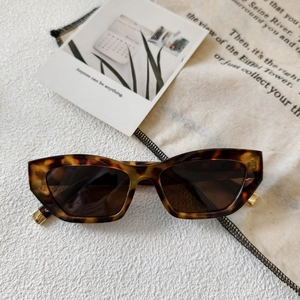 Retro cat-eye sunglasses with tortoise frame and gold hinges on a white stone surface