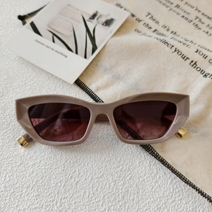 Close-up of nude cat-eye sunglasses with gold metal hinges on a textured surface