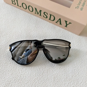 Detail of black square sunglasses with gold metal hinges and dark lenses on a white background