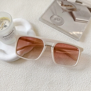 Detailed close-up of square cream sunglasses with stylish pink gradient lenses and metal bridge