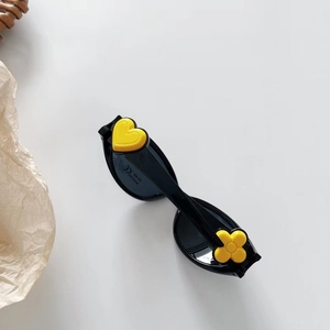 Détail de lunettes de soleil noires pour enfants avec motifs cœur et fleur jaunes
