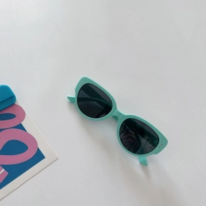 Detail of mint green cat-eye sunglasses with silver dot accents and dark lenses