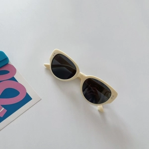 Retro cream oval kids sunglasses with dark lenses and silver dot details on white background
