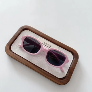 Pink silicone polarized children's sunglasses in a wooden tray on a white background