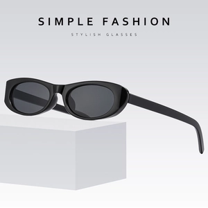 Minimalist black oval cat-eye sunglasses with dark grey lenses on white cube display