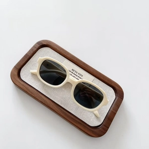 Retro oval kids sunglasses with cream frames and grey lenses on a walnut display tray