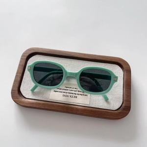 Detail view of foldable mint green kids sunglasses with oval frames on a wooden tray