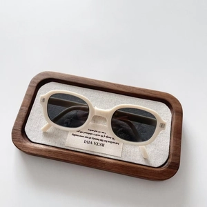 Close-up of cream children's folding sunglasses in a wooden tray with linen texture