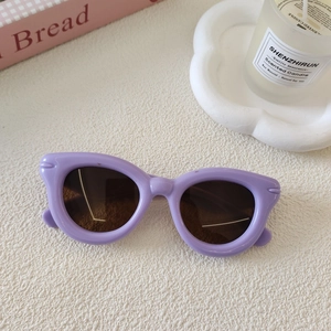 Gros plan de lunettes de soleil violettes pour enfants sur un fond blanc minimaliste et épuré