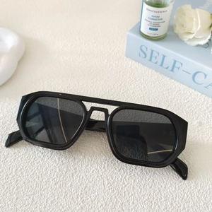 Lunettes de soleil aviateur carrées noires présentées sur un fond avec des accessoires