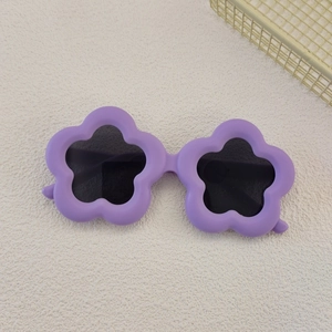 Detailed top view of flower-shaped purple kids' sunglasses on a textured beige sand background