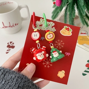 Asymmetric Christmas earrings with Santa and tree charms held by hand against holiday decor