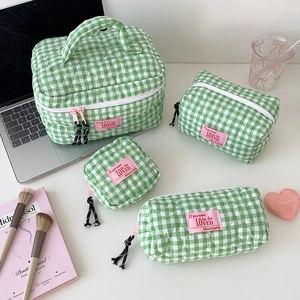 Detailed set of green checkered quilted cosmetic bags with pink labels on white desk