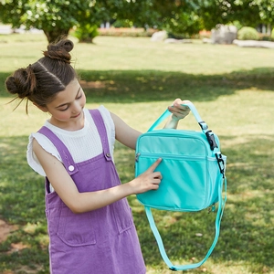 Mint green insulated lunch bag with adjustable blue strap shown by girl in a park