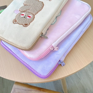 Close-up of plush laptop sleeves with embroidered bear detail and soft faux fur texture