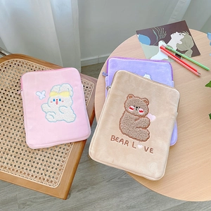 Close-up of plush tablet sleeves with 3D embroidery on woven chair and wood table